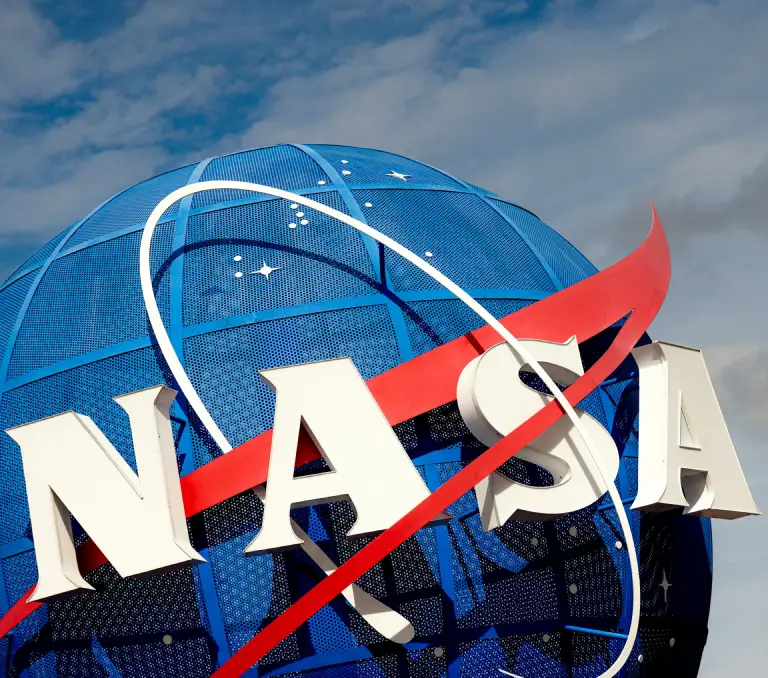 A close-up of the NASA logo at the Kennedy Space Center, with a blue globe and red swoosh design. NASA plays a key role in partnerships with SpaceX for space exploration and Mars missions.