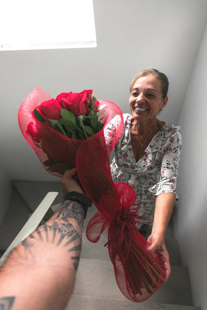 A smiling mother receives a beautiful bouquet of red roses wrapped in elegant red fabric, symbolizing love and appreciation on Mother's Day.