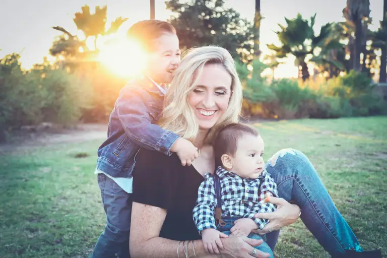 A smiling mother enjoying a sunny outdoor moment with her two young children, symbolizing love, joy, and family bonding on Mother's Day. The warm sunlight and natural setting capture the essence of celebrating motherhood.