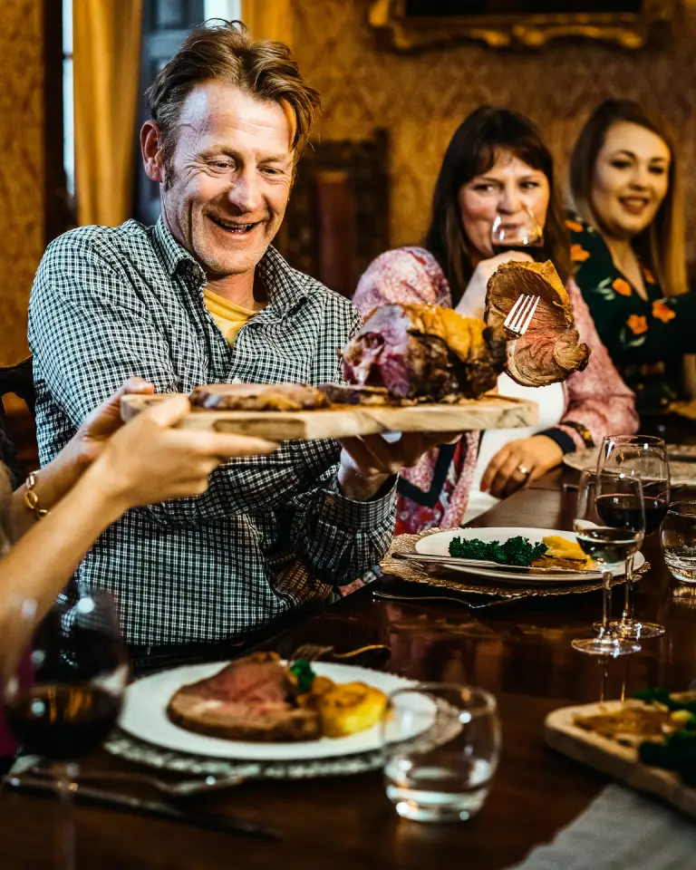 A joyful family gathered around a beautifully set dinner table, enjoying a hearty roast meal with wine and laughter. This warm and festive moment captures the essence of celebrating special occasions like Father's Day, bringing loved ones together for a memorable feast.