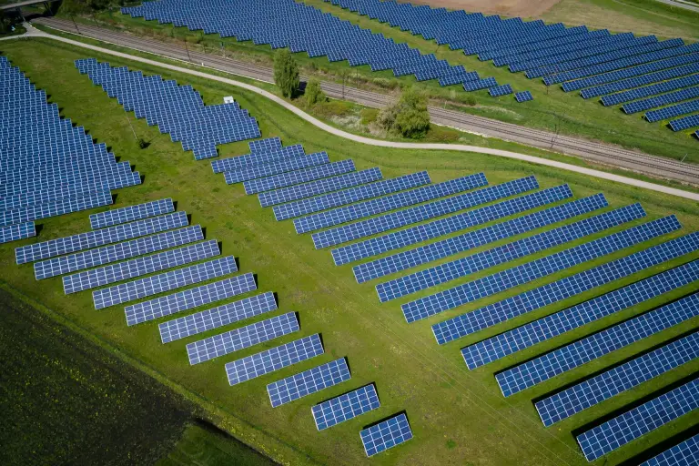 Aerial view of a large solar panel farm with neatly arranged rows of solar panels on green fields, representing the expansion of renewable energy supported by solar incentives in the UK.